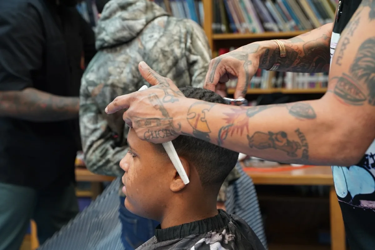 Close view of a barber's hands shaping a student's haircut.