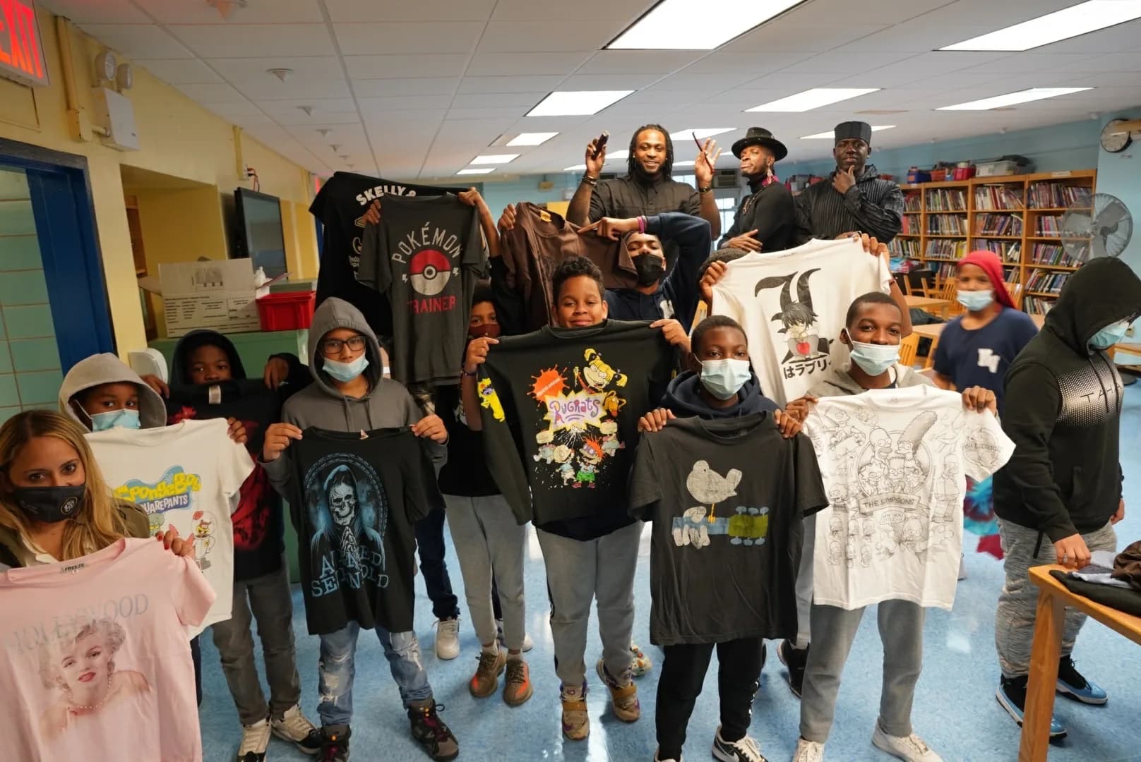 Group of students and adults holding vintage T-shirts in a school library.