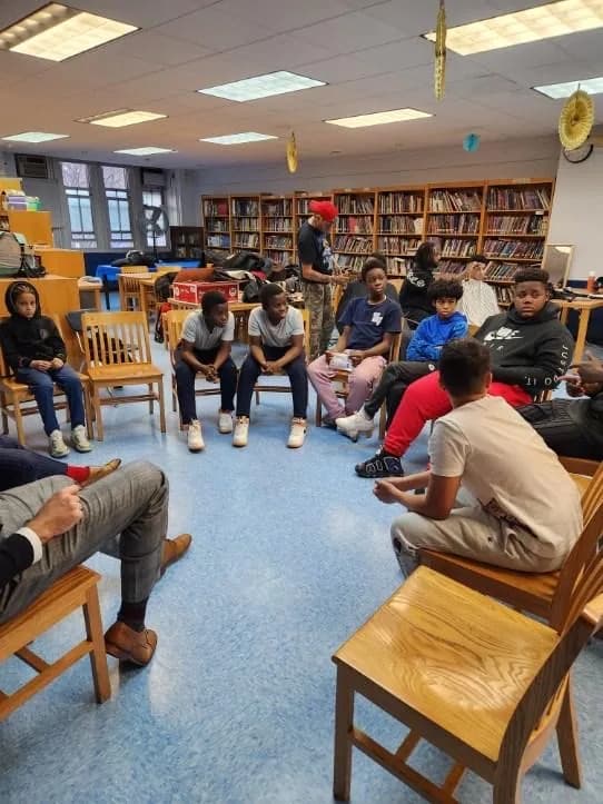 Students and adults seated in a discussion circle inside a classroom.