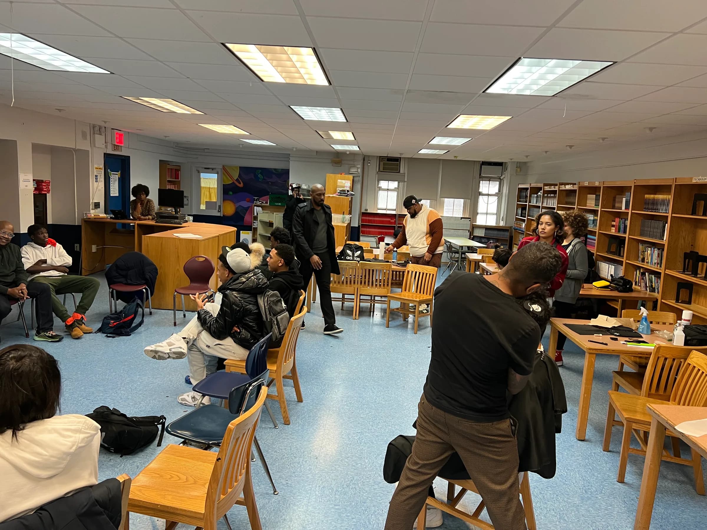 Community discussion and barbering activity taking place in the same school room.